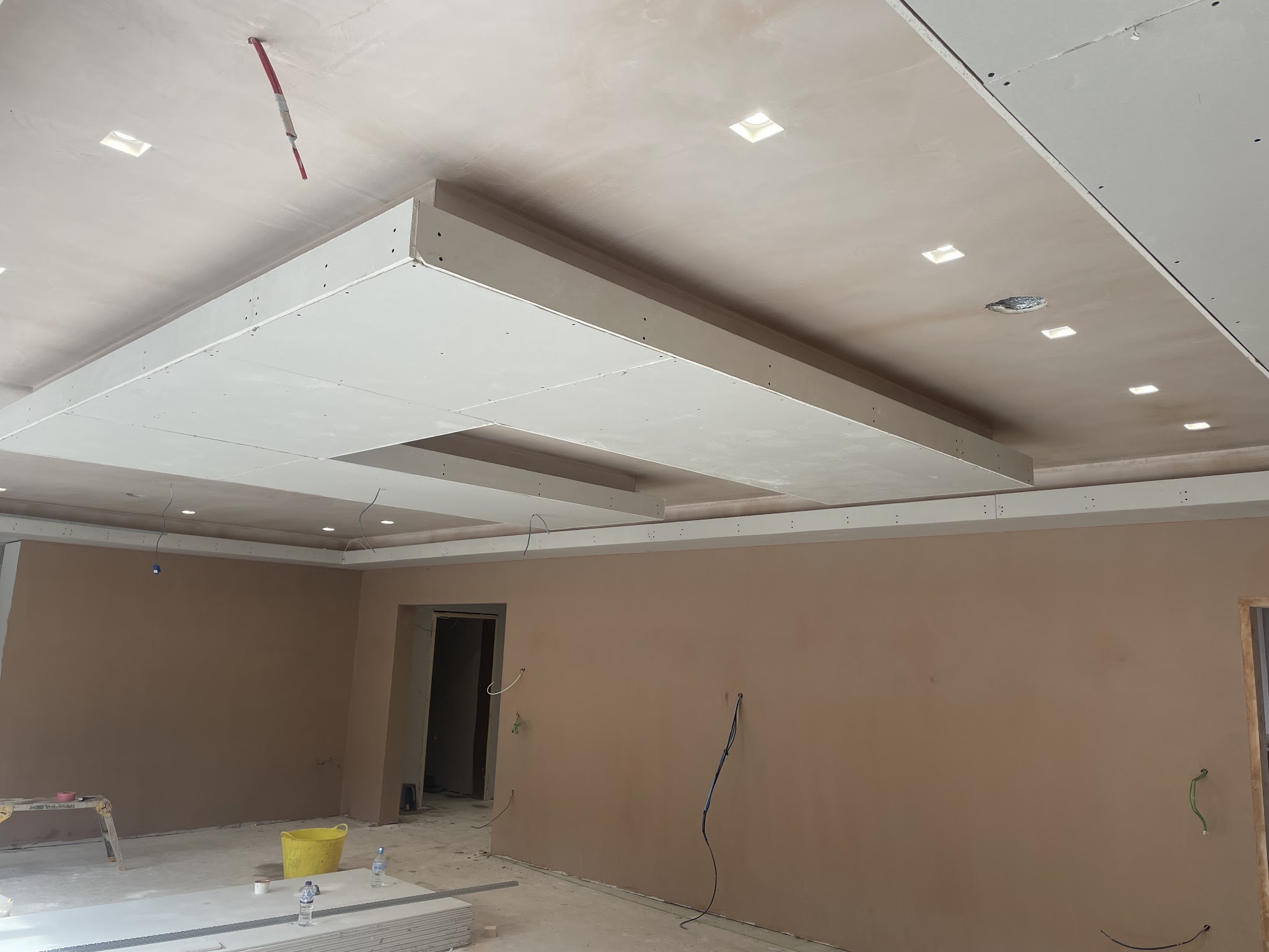 A finished plastered ceiling with a recessed panel and spotlights in a large room
