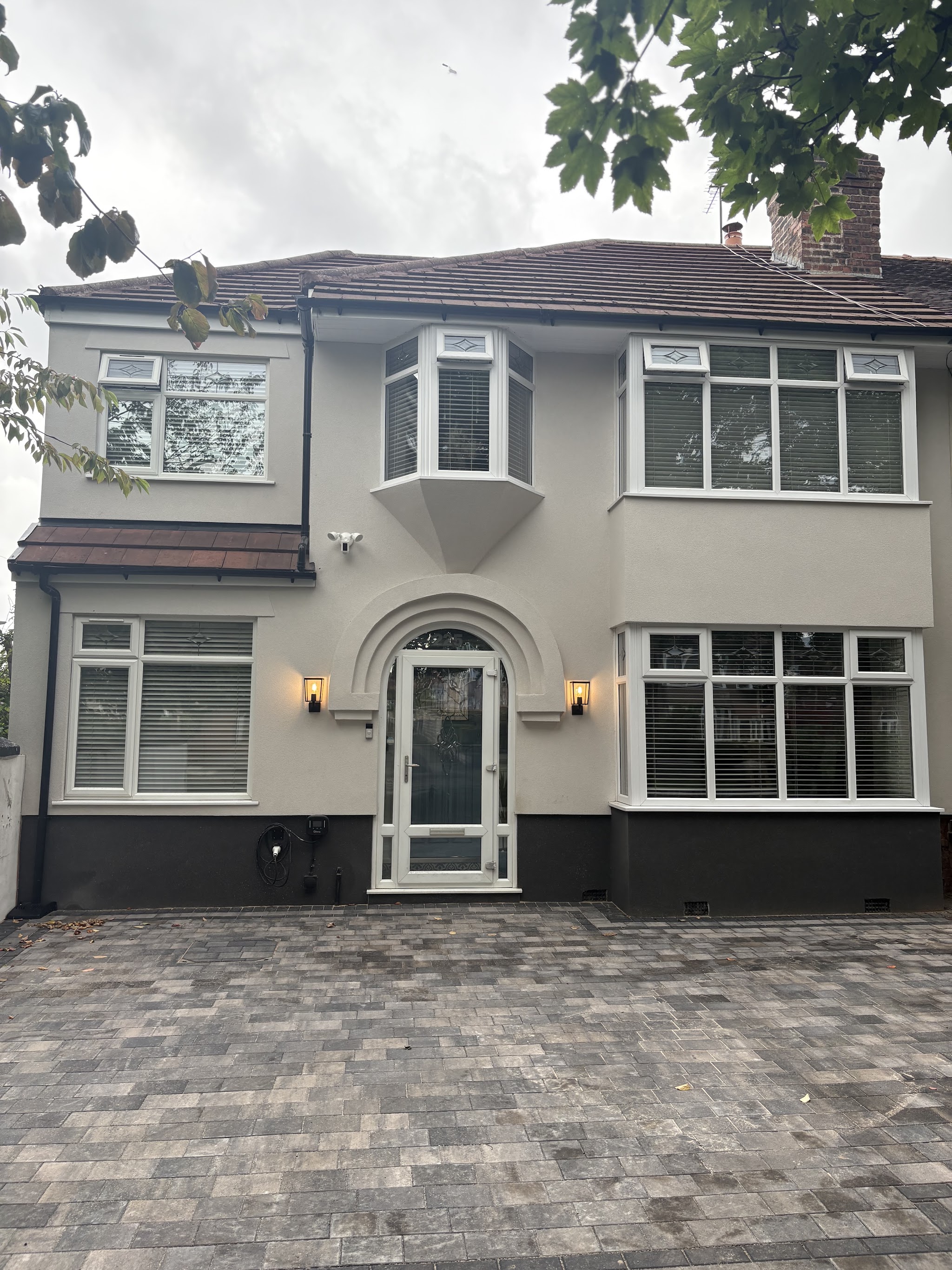 A finished cream rendered semi-detached house with a dark plinth and bay windows