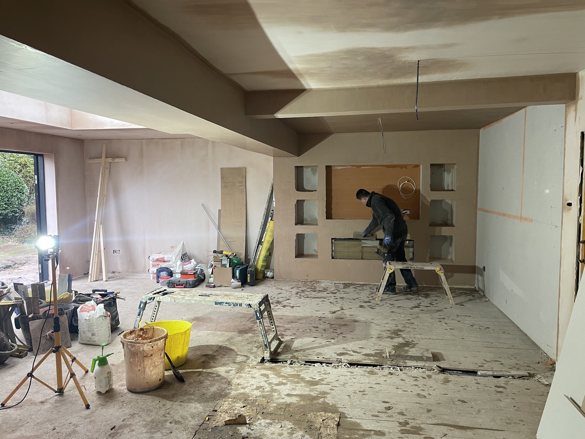 Plastering under way in a large open room, with a plasterer at work